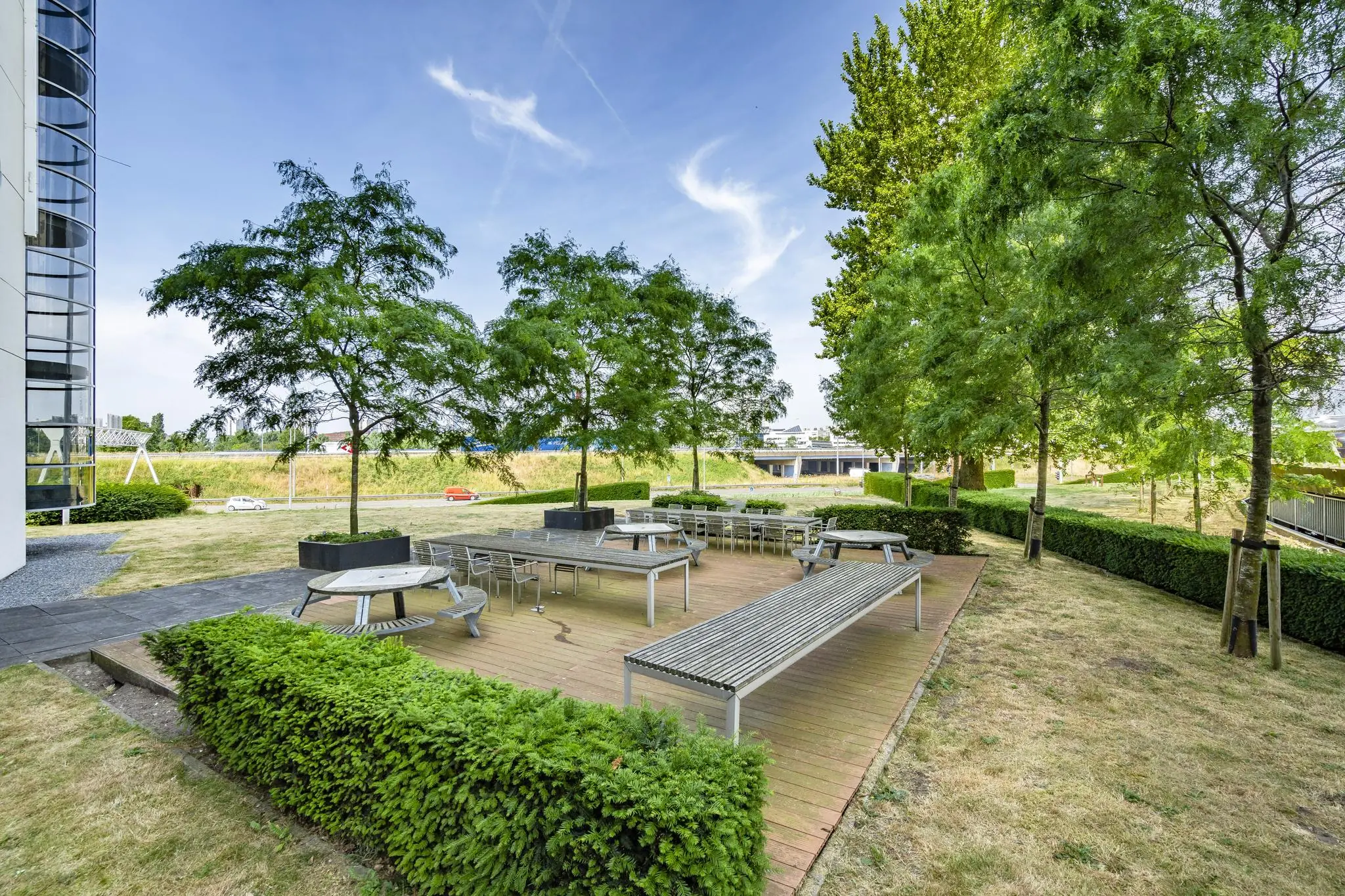 Buitenterras met tafels en banken tussen groene bomen bij Rivium Quadrant.
